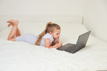 Little girl with laptop lying on bed