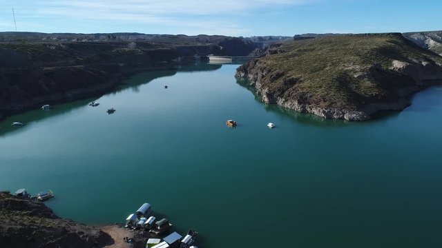 Aerial drone scene of Agua de Toro dam. Flying over the lake, passing near boats. Semi circular concrete structure at background. San Rafael, Mendoza, Cuyo Argentina.