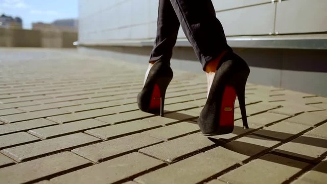 female feet booted fashionable high heels shoes are stepping on tiled surface outdoors in sunny day