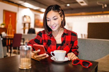 Young pretty brunette hipster happy girl using smartphone sitting with coffee in cafe