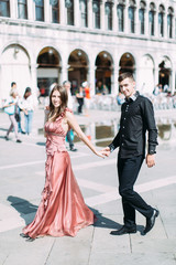 Romantic couple walking on Piazza San Marco in Venice. Pretty girl in pink dress and handsome boy in black clothes