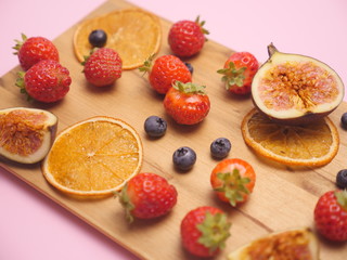 Fresh fruits on wooden plate. Fruit p;ate with strawberry, blueberry, sweet cherry on wooden background. Flat lay, top view. Assortment of juicy fruits on wooden table, on bright background.