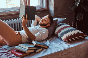 Portrait of a handsome student guy reading a book in his bed. Education concept.