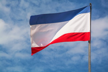 The national flag of the Republic of Crimea is fluttering in the wind against the sky