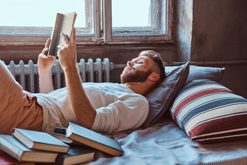Portrait of a handsome student guy reading a book in his bed. Education concept.