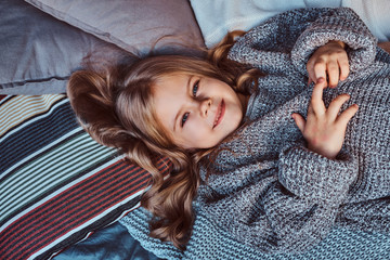Close-up portrait of a little girl in warm sweater lying on bed.