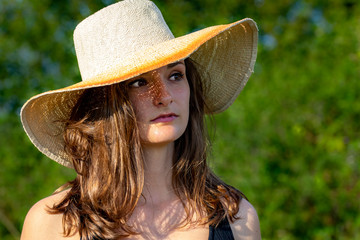 portrait d'une jeune femme brune au cheveux longs en robe noire sous un grand chapeau de paille...