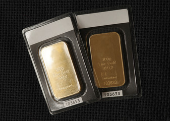 Two minted gold bars weighing 100 grams each against the background of a dark fabric texture.