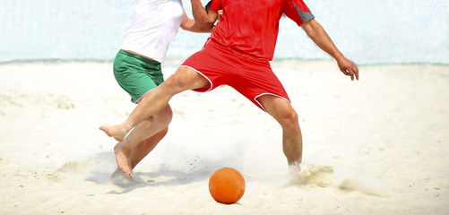 Close-up of players foots playing football on sand