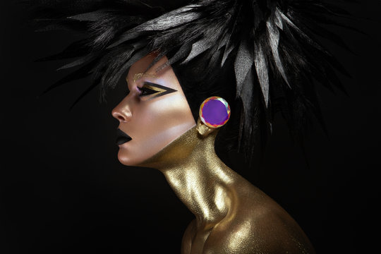 Studio beauty portrait of young woman with black graphic makeup, gold body and fashion haistyle