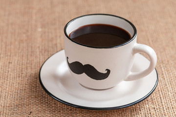 Cup of coffee with mustache on burlap background. movember