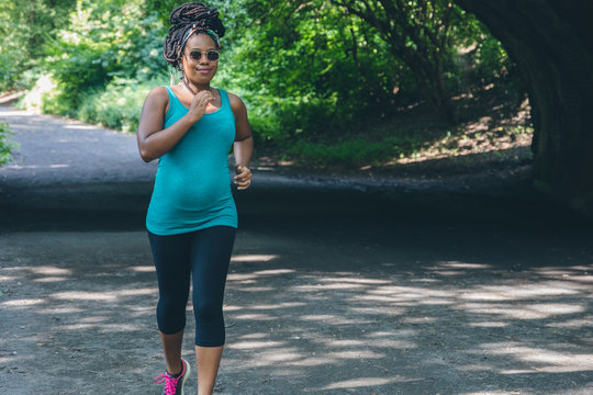 Pregnant woman with dreadlocks jogging on country road