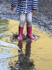 Playful child outdoor jump into puddle in boot after rain
