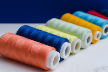 Various colored spools of sewing thread lie on a wooden table