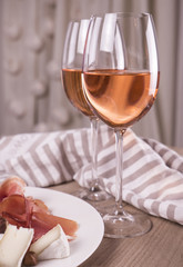 Rose wine and snacks. Two glasses rose wine on wooden table. Plategreen olives, hamon and cheese on wooden table. Glass of rose wine served with cheese plate. French wine with homemade cheese.