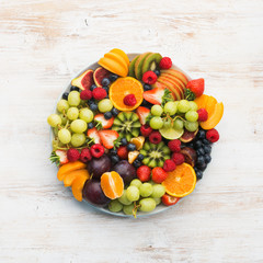 Healthy fruit platter, strawberries raspberries oranges plums apples kiwis grapes blueberries on the white wooden table, top view, copy space for text, square, selective focus