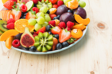 Healthy fruit and berries platter, strawberries raspberries oranges plums apples kiwis grapes blueberries on the light wooden pine table, close up, copy space for text, selective focus