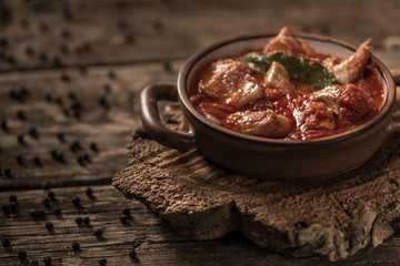 Delicious meat and tomato meal served in small ceramic baking dish with handles on wooden table background