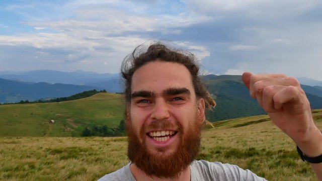 A man does selfie in the mountains. Joyous video, turn in a circle