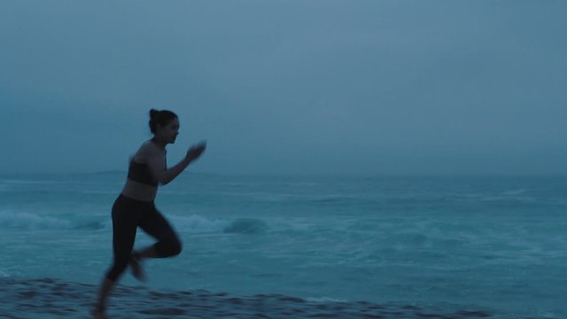 fit young woman running on stormy beach sprinting fast exercising cardio endurance training focused female athlete runner in cloudy seaside
