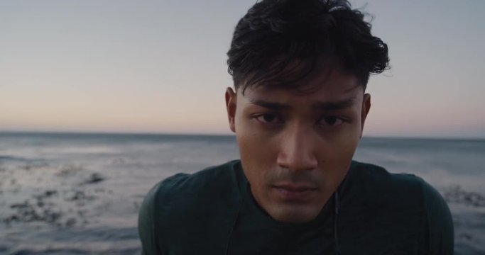 attractive young runner man resting after running workout on seaside fit asian athlete exhausted looking tired at camera ocean sunrise background