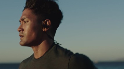 fit young man running athlete runner training tough cardio exercise workout on calm ocean seaside run wearing earphones at sunrise close up slow motion