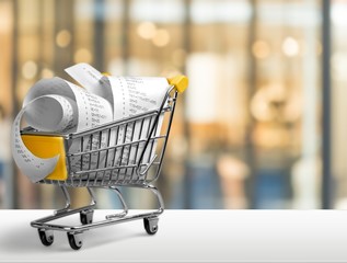 Shopping cart full with bills on background