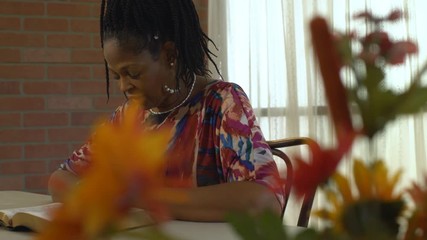 With colorful flowers in the foreground scene tracks by a lovely Christian African American woman who is spending quiet time reading her Bible.