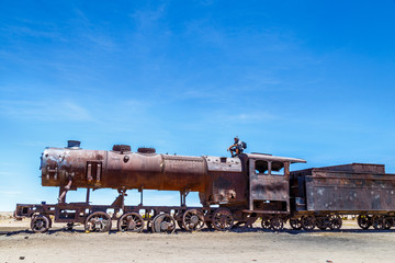 Fototapeta na wymiar Homme assis sur vieux train rouillé métal dans le désert de sel de Bolivie Cimetière