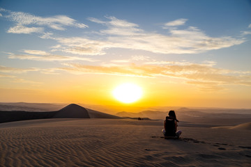Fototapeta na wymiar Femme assise qui regarde le Coucher du soleil dans le désert Huacachina Ica au Pérou Voyageuse aventurière paysage