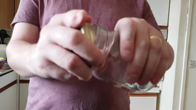 Male with a partially amputated index finger on his right hand removes the lid from a glass jar
