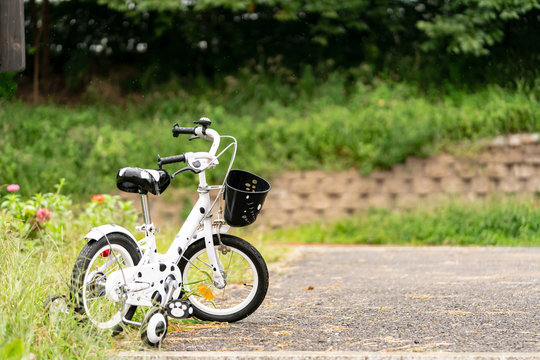 Sidewalk bike is stand alone on the side of road. This has training wheels at rear side to ease riding for children and black basket on the front side.