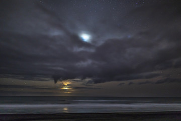 Fototapeta premium A crescent moon iluminates the coastline and sea landscape during twilight hour at 