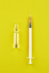 Ampoule with medicine and syringe on yellow background