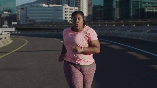fat african american woman running exercising intense weight loss workout jogging in urban city background at sunrise wearing earphones