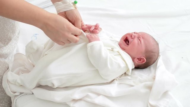 Nursing mother dressing her newborn crying baby in maternity