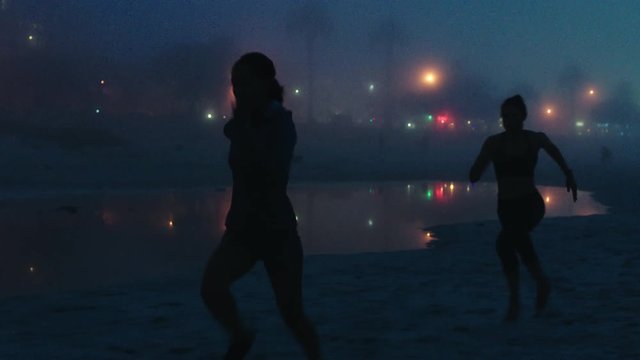 silhouette of women running athletes training sprinting exercise intense fitness challenge on misty beach evening at night