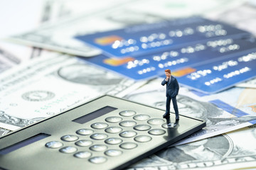 Credit card debt, financial problem or loan payment concept, miniature people businessman standing and thinking worry about debt with calculator on US Dollar bills money and credit cards