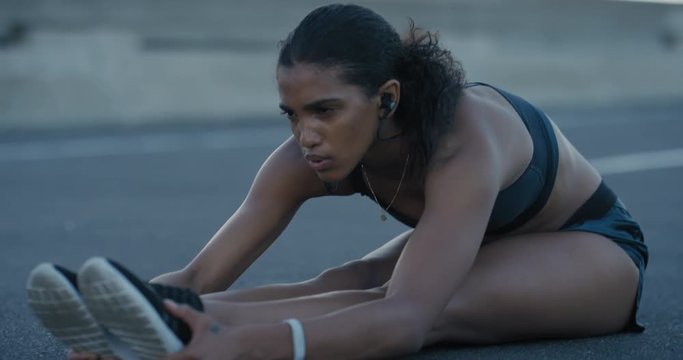 young hispanic woman runner stretching warm up exercise preparing for running workout in city at sunrise wearing earphones fitness listening to motivation music