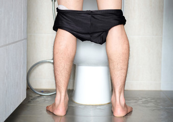 Rear view Leg of man standing peeing to toilet bowl in restroom at home  . Health concept