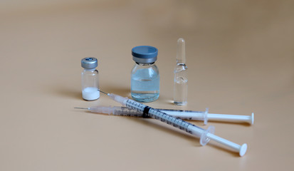 The vial and disposable syringe against a soft brown background.
