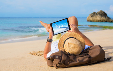 Fototapeta na wymiar Man buying airline tickets online on tablet while relaxing on beach