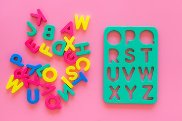 Alphabet for kids concept. English letters in disorder near stencil on pink background top view