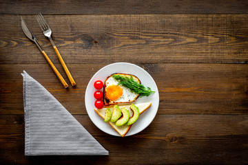 Healthy hearty breakfast. Fried eggs with vegetables near toast with avocado on dark wooden background copy space