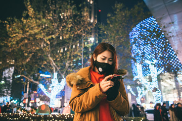 Obraz premium Young asian girl wearing a mouth mask with smart phone and winter festive on the background