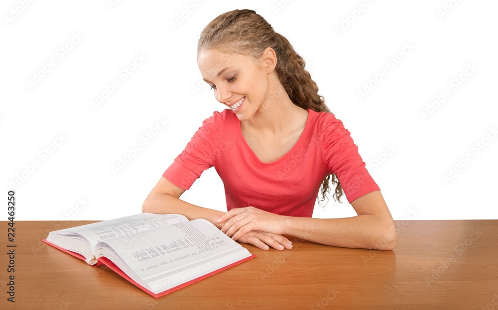 Wall mural Friendly Young Girl Sitting Behind a Desk and Reading a Book -