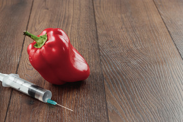 Red pepper and stuck in it a syringe on a wooden background. Concepts of genetic modification....