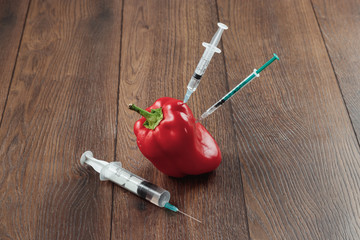 Red pepper and stuck in it a syringe on a wooden background. Concepts of genetic modification. Products of GMOs