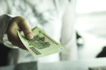 Close up of asian woman's hand holding vietnam bank note make payment at shop or supermarket. Asia...