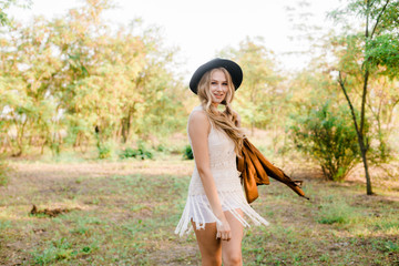 Beautiful young girl with blond hair in a suede jacket with fringed and black felt hat in the...